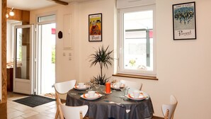A dining area with a table set for four, white chairs, a potted plant, and artwork on the walls.
