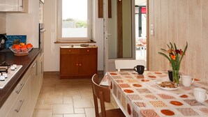 A modern kitchen with a dining area, featuring a window, a bowl of oranges, and a table set for two.