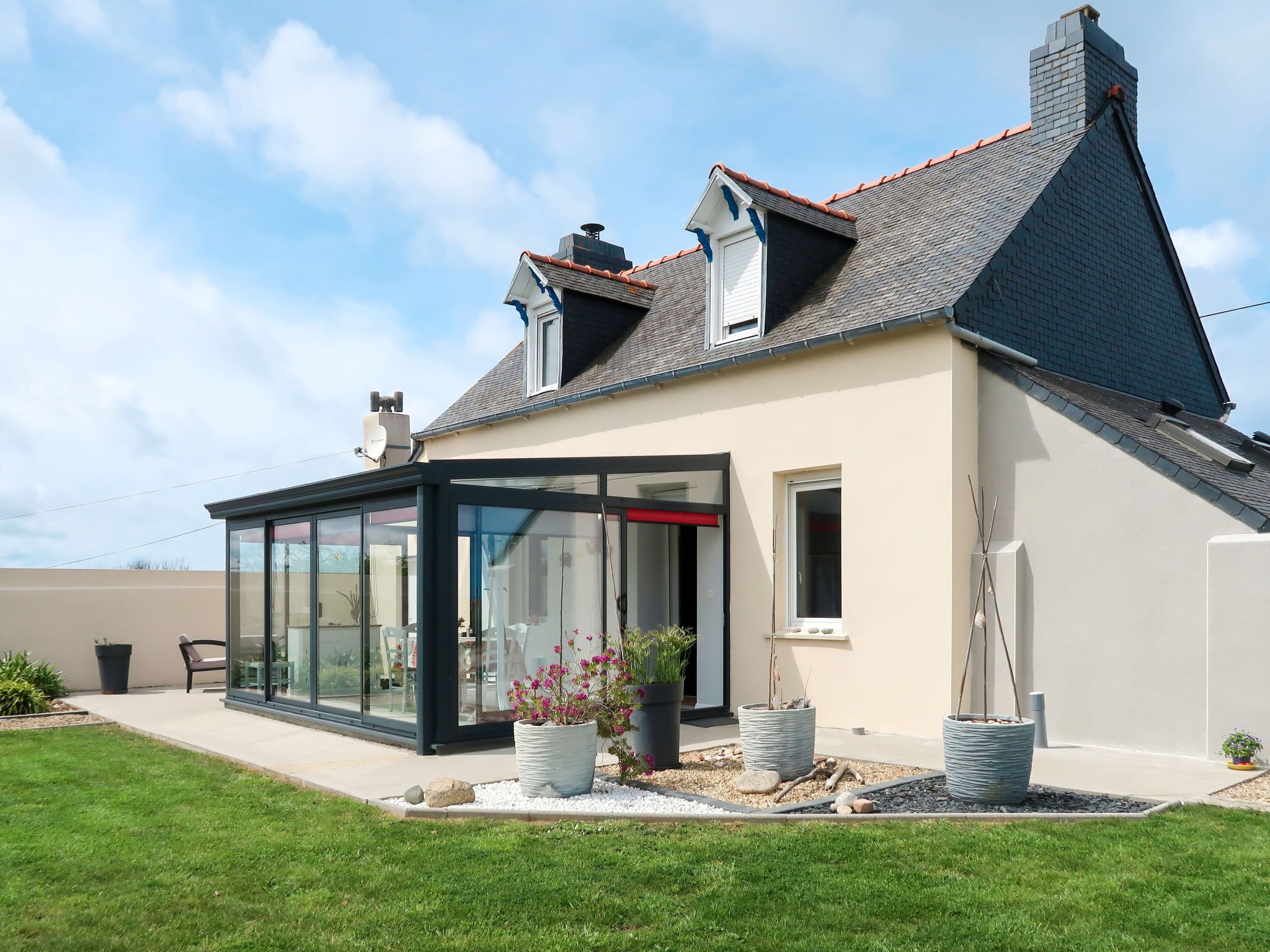 A modern house with a glass-enclosed patio, a sloped roof, and a well-maintained garden.