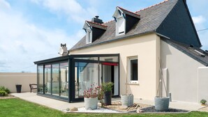 A modern house with a glass-enclosed patio, a sloped roof, and a well-maintained garden.