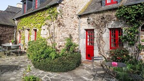 A stone building with red doors and windows, a stone staircase, and outdoor seating. - Dolce Vita by Interhome (Plouha)