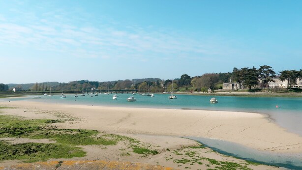 A coastal scene with a sandy beach, boats on calm waters, and buildings in the background. - Pors Ar Goff by Interhome (Plestin les Greves)