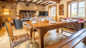 A cozy dining area with a stone fireplace, wooden beams, and a television. - Pors Ar Goff by Interhome (Plestin les Greves)