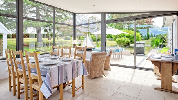 A dining area with a large glass wall, wooden chairs, and a table set for four. - Chante-Brise by Interhome (Plérin)