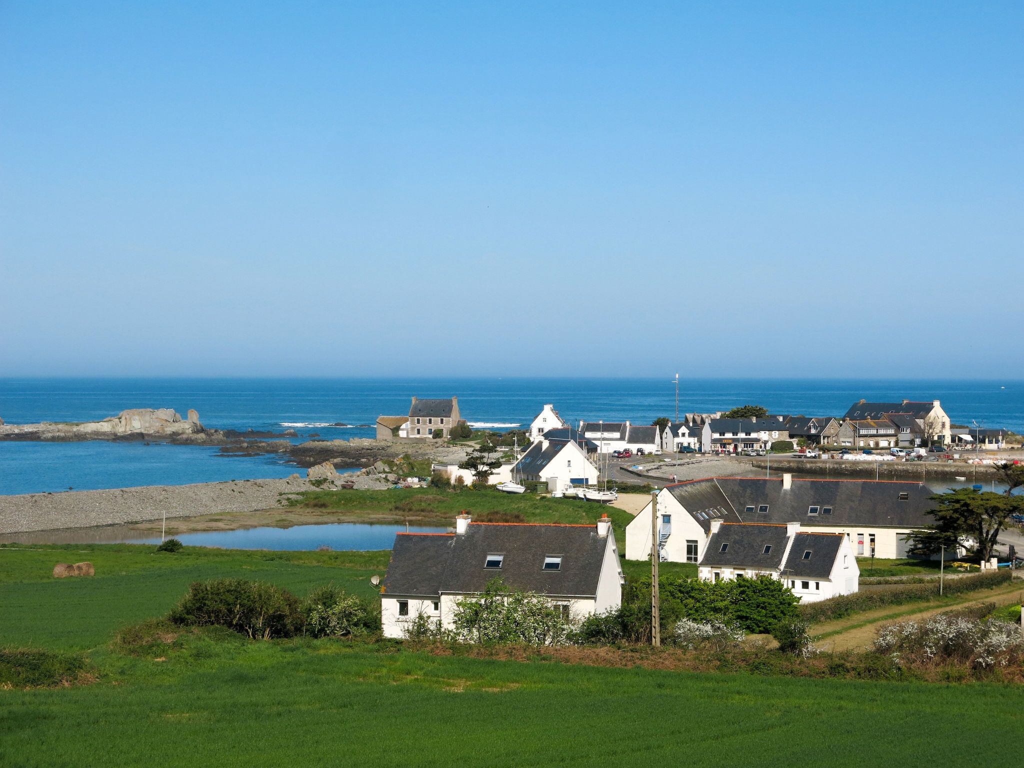 Ein Küstendorf mit weißen Häusern, blauem Himmel und dem Meer im Hintergrund.