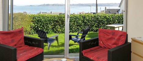Un balcón con mobiliario de mimbre, una mesa de vidrio y vista al mar.
