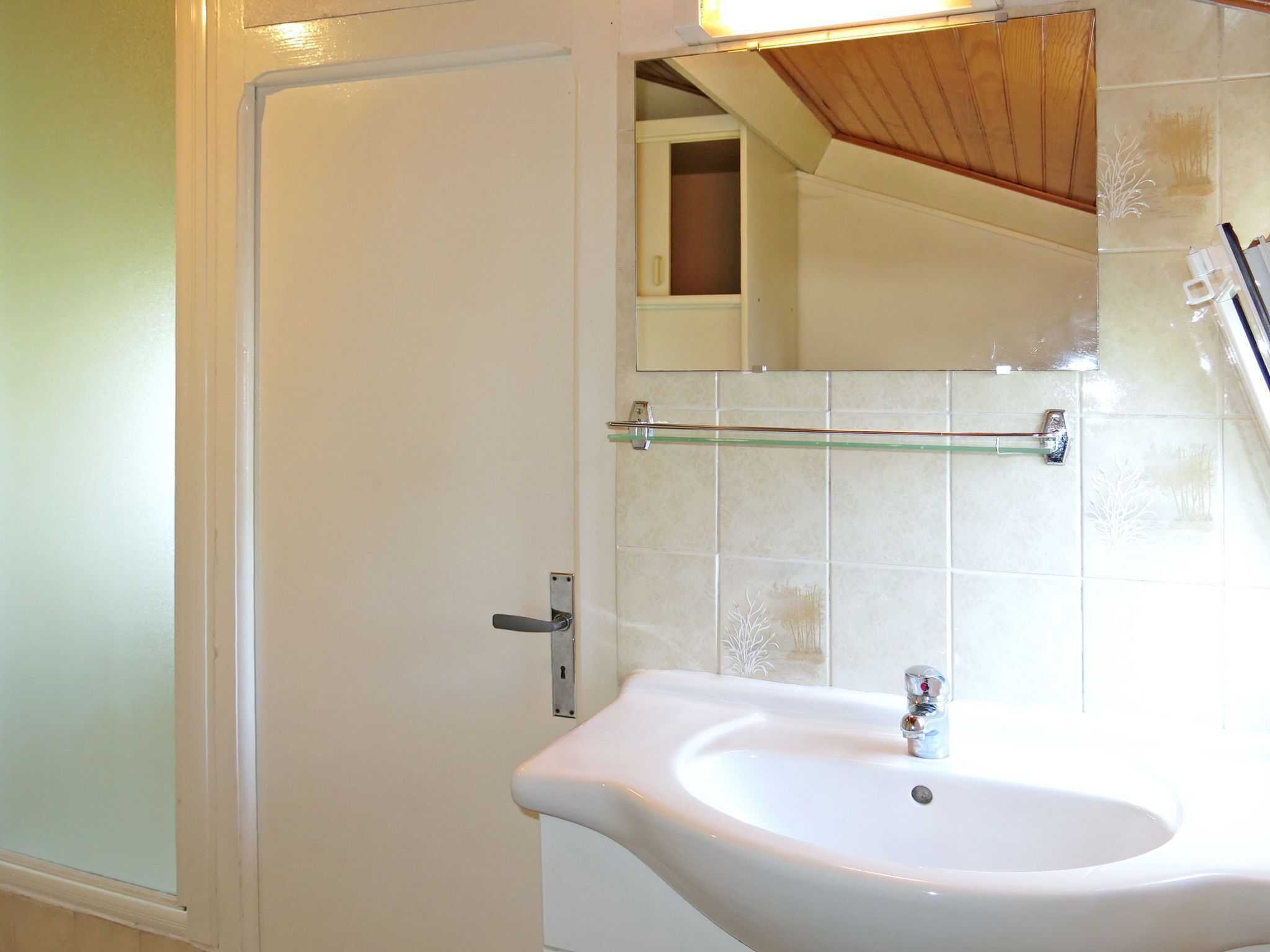 Een badkamer met een wit wastafelmeubel, een glazen plank en een spiegel.