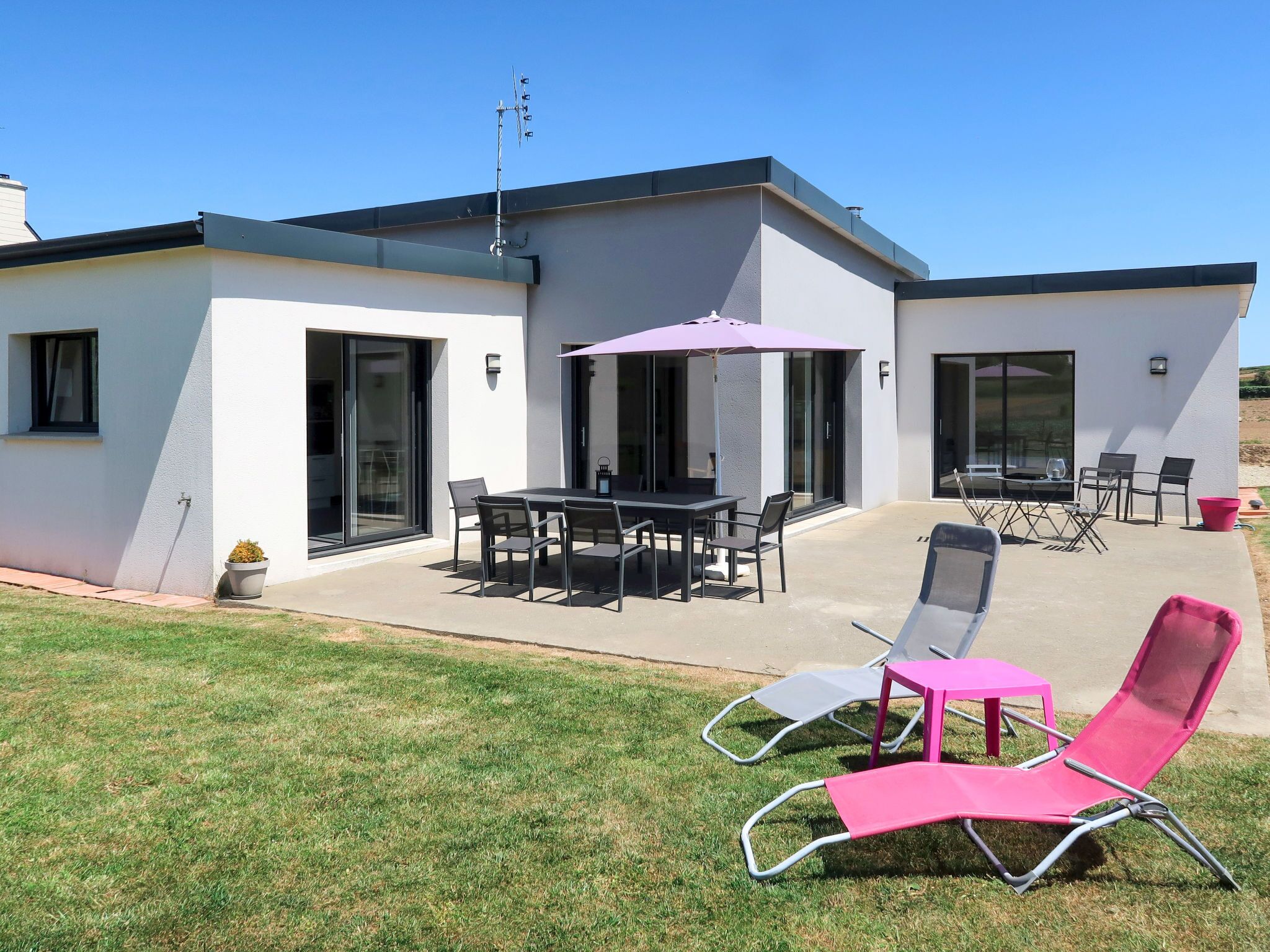 A modern house with a patio, a dining area, and two lounge chairs.