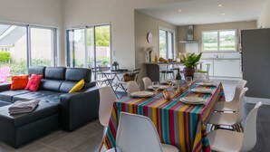 A modern living room with a black sofa, a dining table with a colorful striped tablecloth, and a kitchen area with white cabinets and a black refrigerator. - Terre et Mer by Interhome (Treflez)