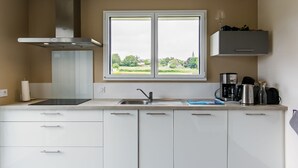 A modern kitchen with a window, white cabinets, and a stainless steel range hood. - Terre et Mer by Interhome (Treflez)