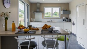 A modern kitchen with a large island, white cabinetry, and a view of greenery outside. - Terre et Mer by Interhome (Treflez)