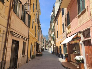 A narrow street lined with colorful buildings, some with balconies and awnings, leading towards a distant mountain.