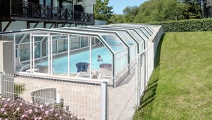 Un bâtiment moderne doté d’une piscine intérieure à panneaux de verre, d’un espace extérieur aménagé et d’une pelouse bien entretenue.
