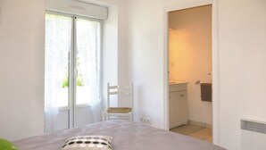 Een slaapkamer met een bed, een stoel, een badkamer en een raam met gordijnen.