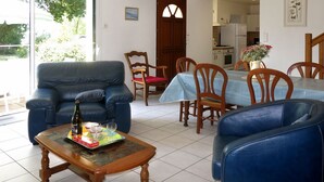 Een woonkamer met een blauwe leren bank, een houten salontafel en een eetgedeelte met een blauwe tafelkleed en houten stoelen.
