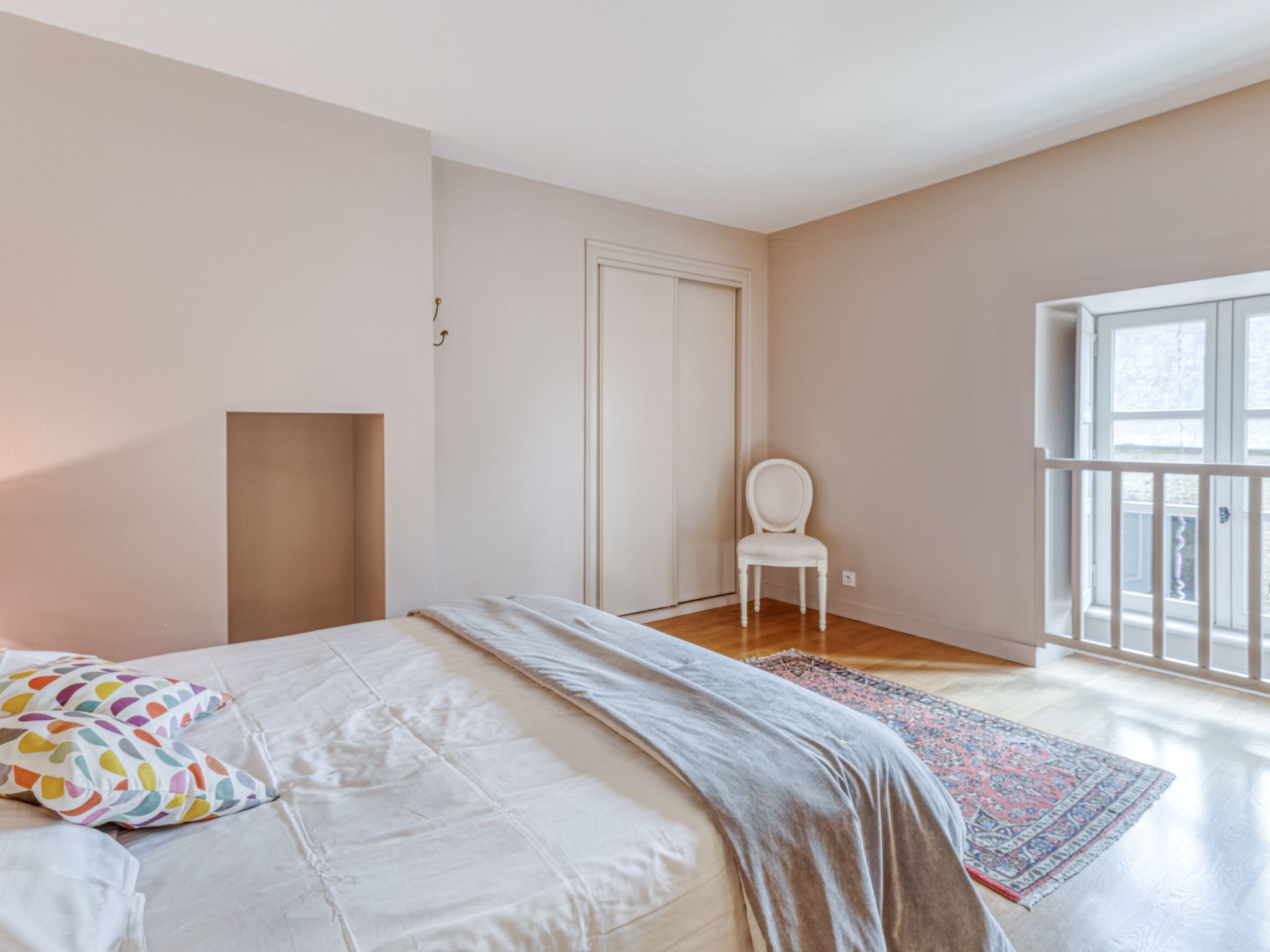 Une chambre à coucher avec un lit, une chaise, une porte et une grande fenêtre.