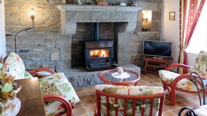 Un salon chaleureux avec une cheminée en pierre, des fauteuils confortables et un téléviseur.