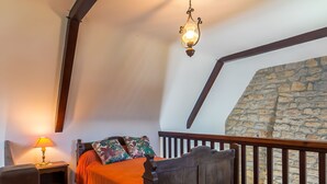 Une chambre à coucher avec un lit en bois, une table de chevet, une lampe, un tapis rouge et un mur en pierre.
