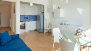 A modern kitchen with white cabinets, a blue backsplash, and a glass dining table.