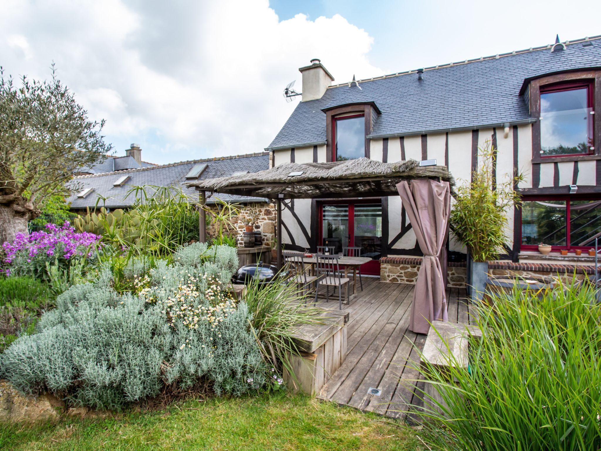 A house with a wooden deck, a thatched roof, and a stone wall.
