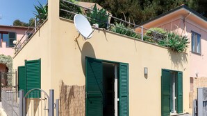 Ein kleines Gebäude mit Satellitenschüssel, grünen Fensterläden und einem gepflasterten Eingang.