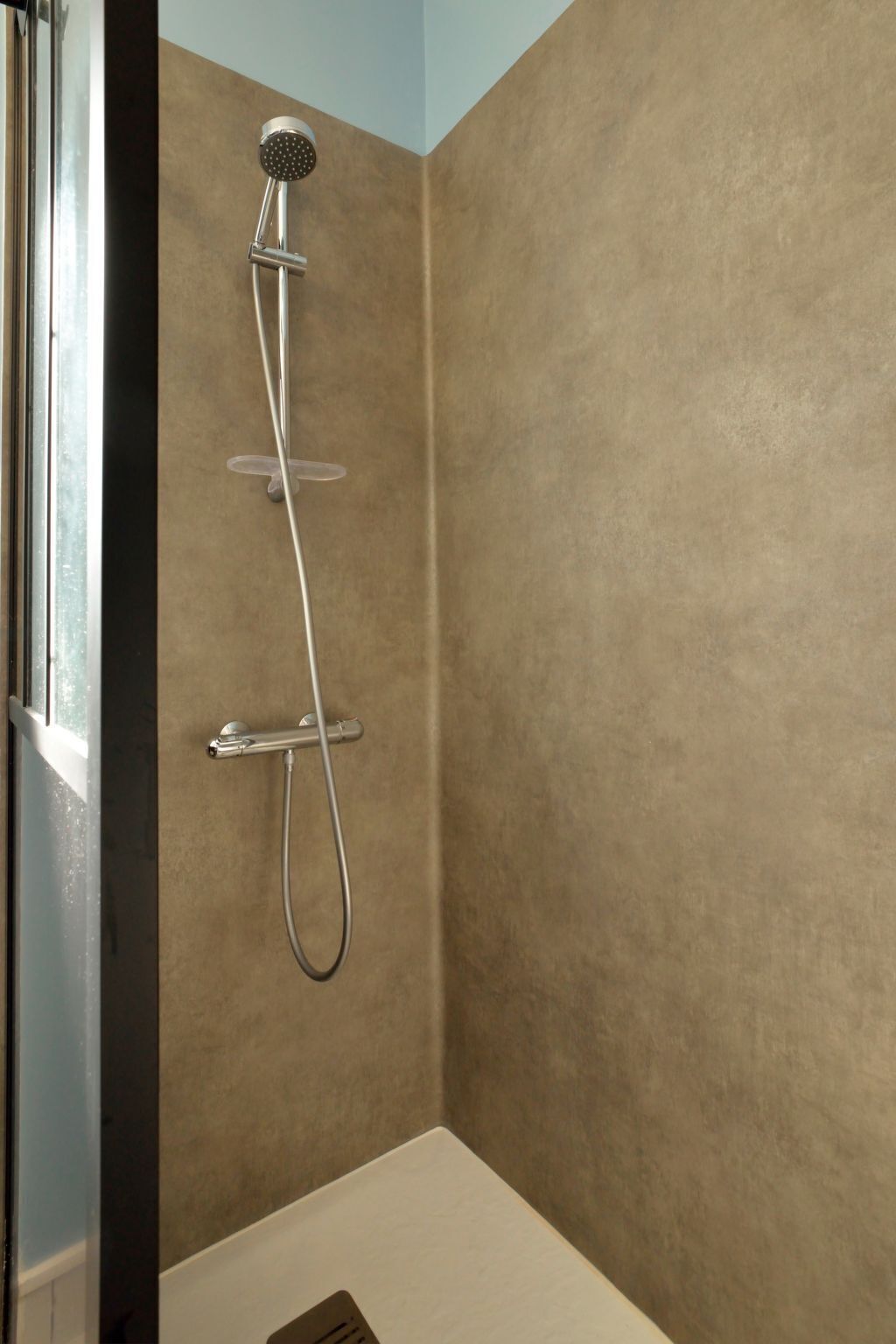 Douche met handdouche en slang, gemonteerd op een wand met een geribbelde beigekleurige afwerking.