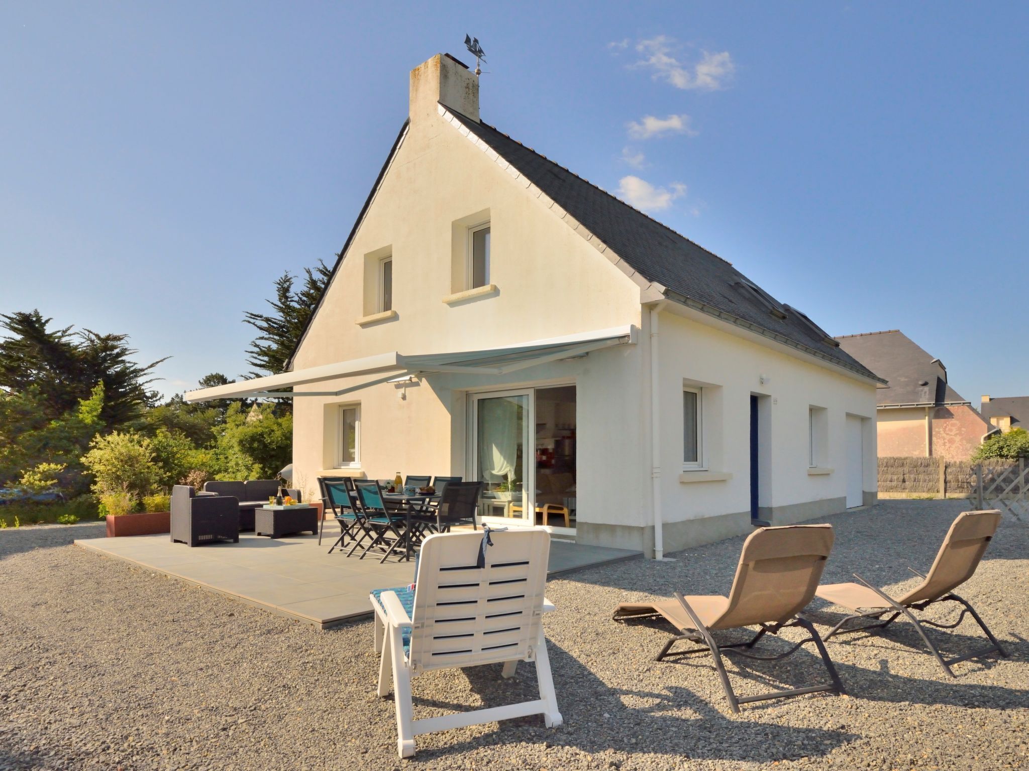 A house with a covered patio, outdoor seating, and a gravel driveway.