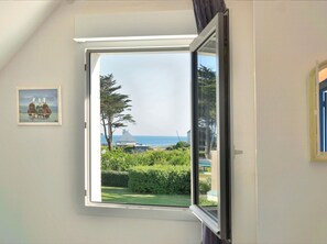 Une pièce dotée d’une grande fenêtre donnant sur la mer et sur un espace verdoyant bordé d’une haie.