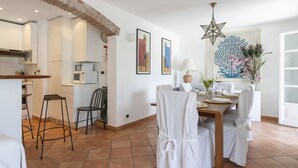 Un comedor con una mesa lista para dos personas, sillas, una lámpara decorativa con forma de estrella y una pared con obras de arte enmarcadas.