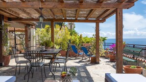 Un patio techado al aire libre con mesa y sillas, plantas en macetas y vista al mar.