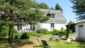 A house with a sloped roof, white exterior walls, and a large tree in the foreground. There are three lounge chairs in the yard. - Stergann by Interhome (Mesquer/Quimiac/Kercabellec)