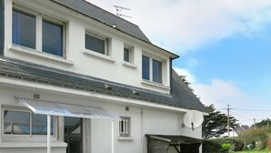 A two-story house with a covered porch, a satellite dish, and a small garden area with two lawn chairs.