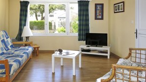 A living room with a sofa, a television on a stand, a small table, and a window with curtains.