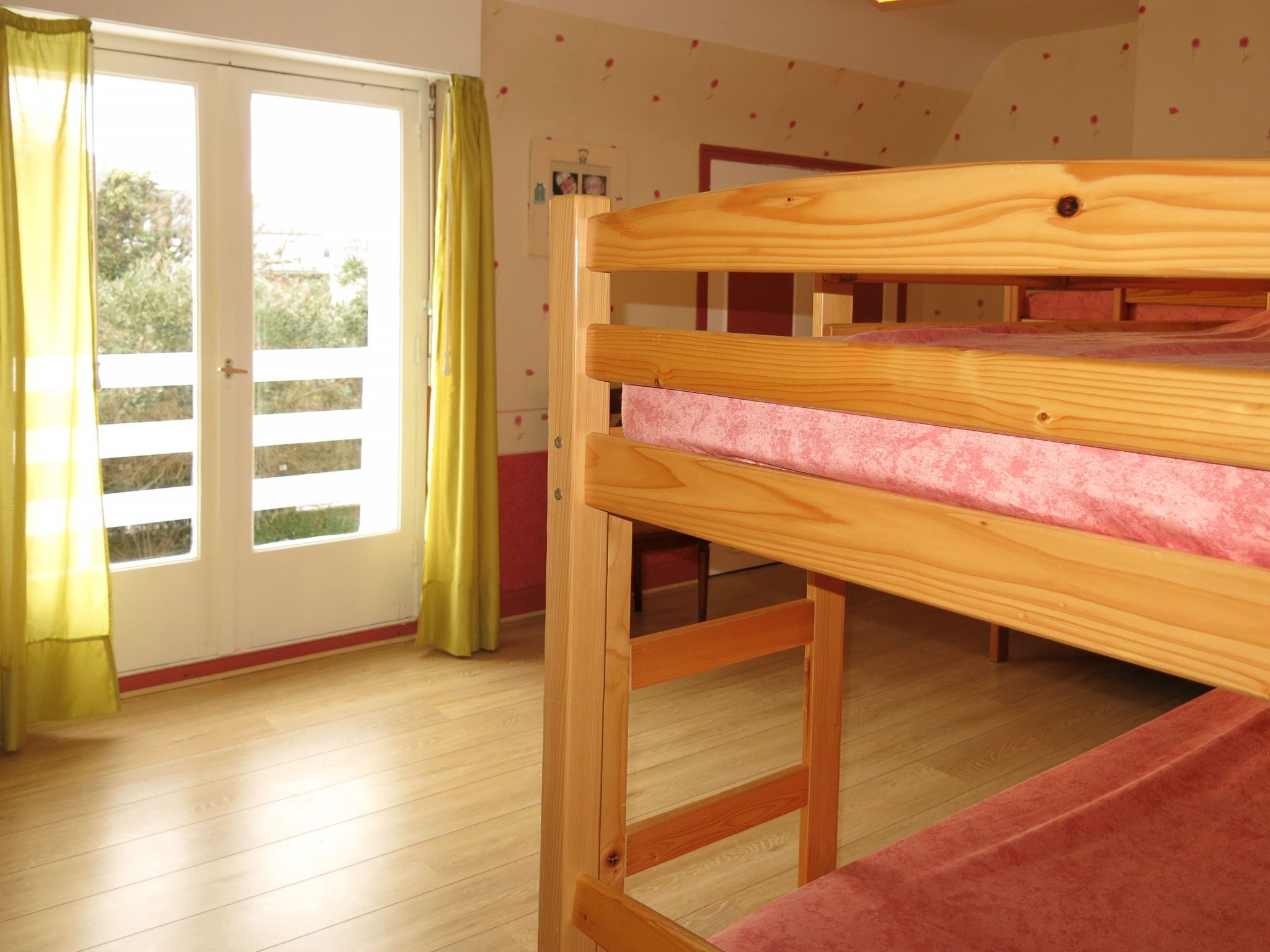 A bunk bed in a room with wooden flooring, a sliding glass door, and a view of greenery outside.