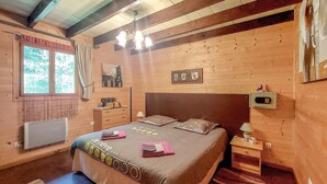 A wooden room with a bed, a nightstand, a lamp, and a window with curtains. - Lovely home in Le Ménil (Le Ménil)