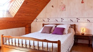 Una camera da letto con soffitto spiovente, una struttura letto in legno, un comodino con una lampada e un pannello decorativo a parete.
