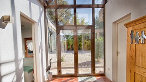 A sunlit entryway with a tiled floor, a wooden door, and a view of a garden through large glass doors. - Alexandre by Interhome (La Chapelle-Saint-Sauveur)