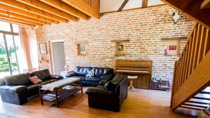 A cozy living room with a brick wall, wooden beams, a piano, and a staircase. - Alexandre by Interhome (La Chapelle-Saint-Sauveur)
