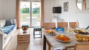 A modern living room with a sofa, a dining table set with seafood, and a TV mounted on the wall. - Le Village de la Mer by Interhome (Talmont Saint Hilaire)