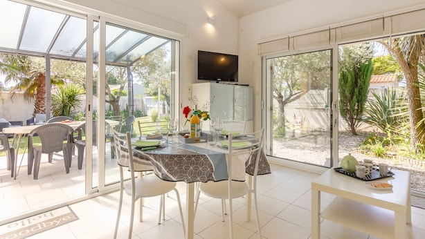 A bright dining area with a glass table, chairs, and a television mounted on the wall. - Les Oliviers by Interhome (Talmont Saint Hilaire)