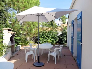 Relax outdoors with a round table and six chairs under a shaded patio surrounded by lush greenery.