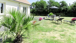 Una casa con techo inclinado, césped y mobiliario exterior, incluyendo sillas y una mesa.