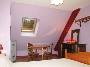 Une chambre avec un plafond en pente, un bureau, deux chaises, un lit, une armoire, un miroir et une fenêtre.