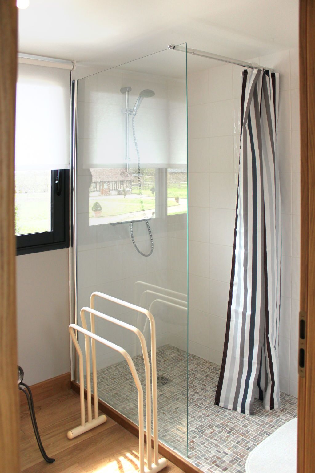 A modern bathroom with a glass shower enclosure, a glass door, a striped shower curtain, and a small window.