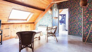 Een gezellig zolderkamer met houten balken, dakraam, eettafel, rieten stoelen en kleurrijke bloemenbehang.
