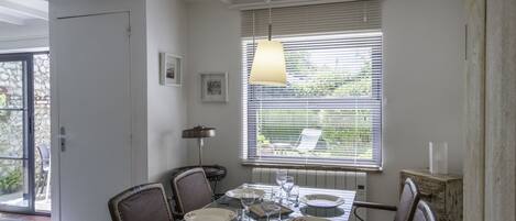 Un coin repas avec une table en verre, des chaises et une fenêtre équipée de stores.