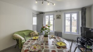 Ein Essbereich mit einem Tisch für zwei Personen, einem grünen Sofa, einem Fernseher und Blick ins Freie.