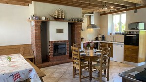 A cozy kitchen with a fireplace, wooden dining table, and modern appliances. - La Bonneraie by Interhome (St.Maurice-en-Cotentin)