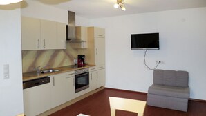 A compact kitchen with a dishwasher, oven, and a coffee maker on the counter. A flat-screen TV is mounted on the wall. - Apartment Huber by Interhome (Zell am Ziller)