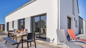 A modern house with a patio area featuring a table, chairs, and lounge chairs.